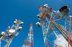 several cellular towers against a blue sky with clouds