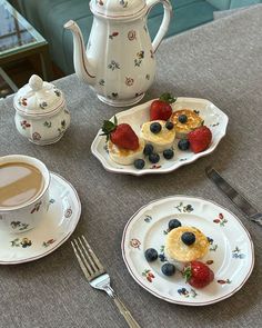 a table topped with plates and cups filled with pastries next to a tea pot