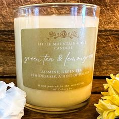 a glass candle sitting on top of a wooden table next to white and yellow flowers