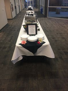 a long table with plates and bowls on it in an office building hallway, decorated with black and white decor