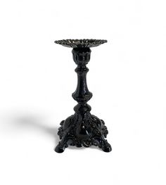 an ornate black candle holder stands on a white background with the light reflecting off of it's base