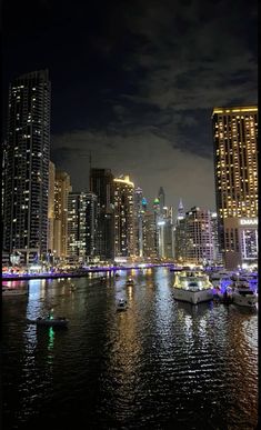 the city is lit up at night with boats in the water