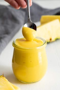 a person is dipping something into a small glass jar filled with yellow liquid and topped with a silver spoon