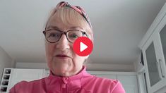 an older woman wearing glasses and a pink top is looking at the camera while standing in a kitchen