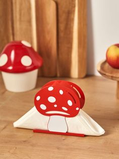 a red and white mushroom sitting on top of a wooden table next to an apple