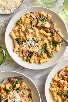 two plates of pasta with mushrooms and spinach on the side next to glasses of water