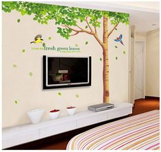 a bedroom with a tree and birds painted on the wall next to a flat screen tv