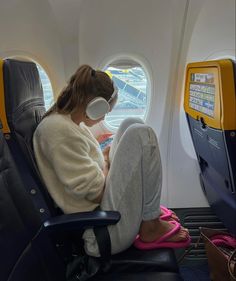 a woman is sitting on an airplane seat with headphones and looking at her phone