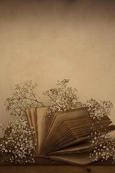 an open book sitting on top of a wooden table next to white flowers and baby's breath