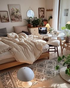 an unmade bed sitting in a bedroom next to a table and chair with potted plants on it