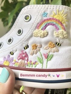 someone is holding up their white shoes with flowers and rainbows on the side, which have been embroidered onto them