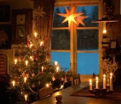 a christmas tree with lit candles is in front of a large window that has a star on it