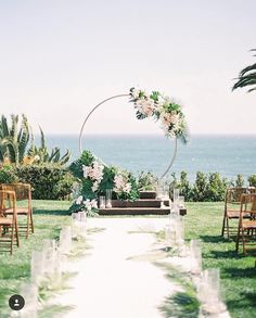 an outdoor ceremony set up with chairs, flowers and greenery in front of the ocean