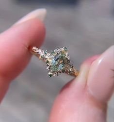 someone is holding an engagement ring with green and white diamonds on it's side