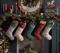 christmas stockings hanging from the fireplace in front of a mantel decorated with candles and wreaths