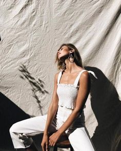 a woman sitting on top of a stool next to a white sheet covered wall with her eyes closed