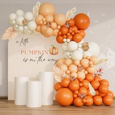 an orange and white balloon arch with pumpkins on the top, as well as other balloons