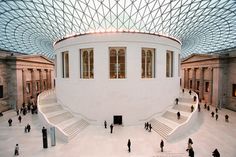 the inside of a building with many people walking around and sitting on benches in front of it