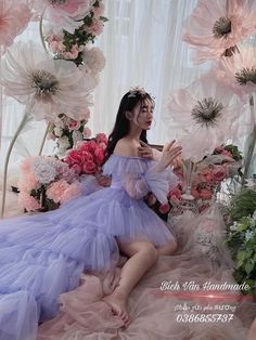 a woman in a purple dress sitting on the ground surrounded by flowers