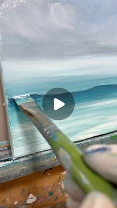 someone is painting an ocean scene on the easel with their paintbrush and brush