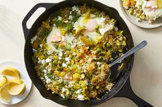 an iron skillet with eggs and vegetables in it next to two plates of lemon wedges