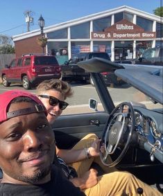 two people are sitting in the driver's seat of a car, smiling at the camera