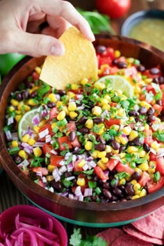 a person dipping a tortilla into a bowl filled with black beans, corn and cilantro