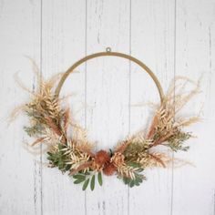 a wreath hanging on the side of a white wooden wall with dried flowers and leaves