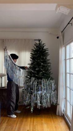 a man is decorating a christmas tree with tinsel and plastic wrapped around it