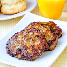 two hamburger patties on a white plate next to orange juice