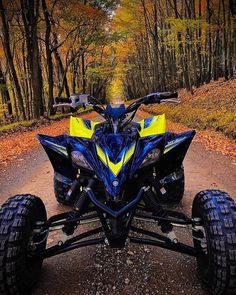 a blue and yellow four - wheeler parked on the side of a dirt road in front of trees