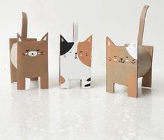 three paper cats are standing next to each other on a white surface and one cat is looking at the camera