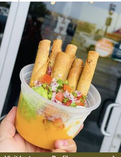 a person holding up a plastic container with food in it that includes pita bread and vegetables