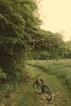 a bike parked on the side of a dirt road next to a lush green field