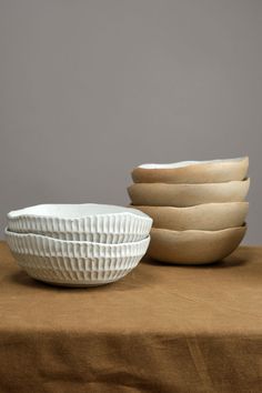 four white bowls sitting on top of a brown cloth covered table next to each other