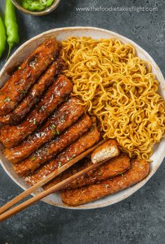 an overhead view of chinese food with chopsticks in the middle and noodles on the side