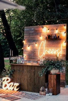 an outdoor bar is lit up with fairy lights and wooden signs that spell out cheers