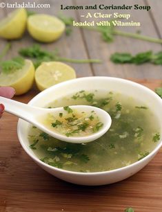 a person holding a spoon full of soup on a cutting board with lemons and parsley