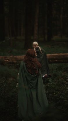 a woman with red hair in a green cloak walking through the woods next to a man