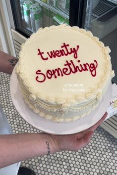 a person holding a cake with the words twenty something on it in front of a refrigerator