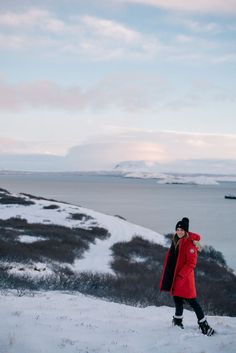 a person standing on top of a snow covered slope next to the ocean and mountains