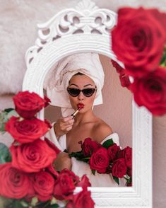 a woman with sunglasses and a towel on her head is brushing her teeth in front of a mirror surrounded by red roses