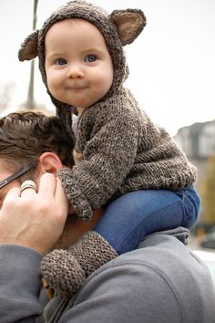 a man is holding a baby wearing a bear hat while he has his eyes closed