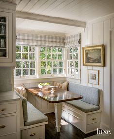 a kitchen with a table and bench in the corner next to two windows that look out onto trees