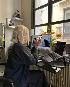 a woman sitting in front of a laptop computer on top of a desk next to a window