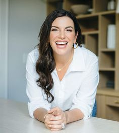 a woman sitting at a table with her hands on her knees and smiling for the camera