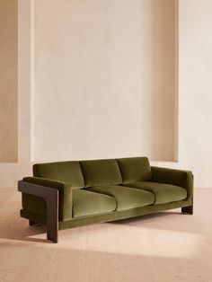 a green couch sitting on top of a hard wood floor next to a white wall