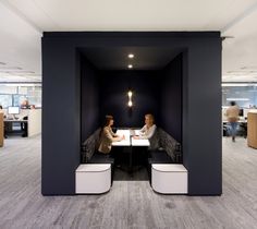 two women are sitting at a table in an office with black walls and white benches