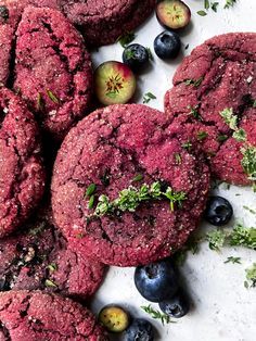 blueberries and plums are arranged on a white surface next to cookies with sprigs