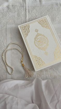 a white and gold wedding card laying on top of a bed next to a tassel